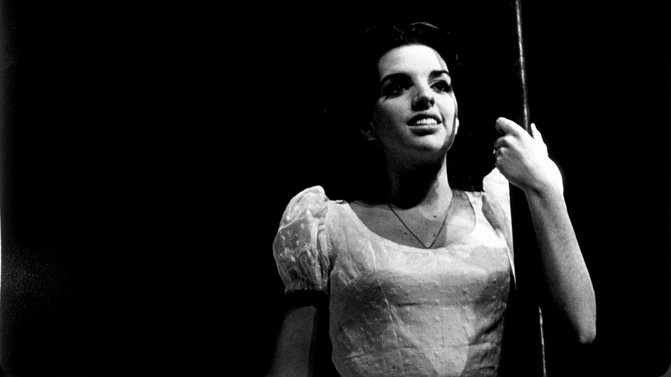 A black and white photo of a woman holding a pole on stage