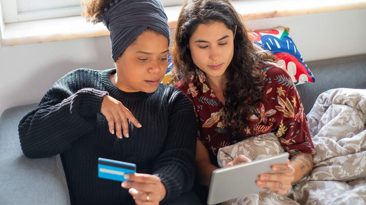 a female couple look at a computer tablet and hold a credit card