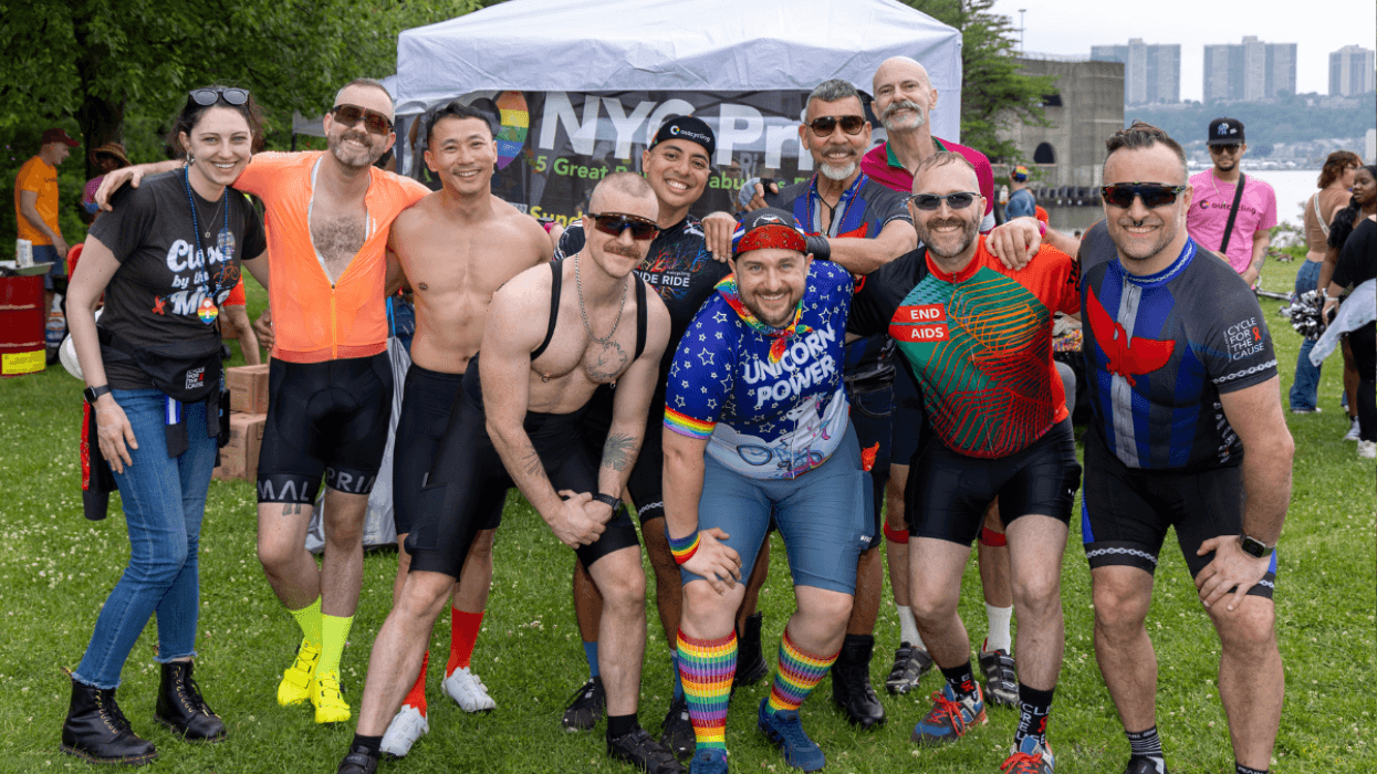 A group of cyclists wearing colorful jerseys and Pride-themed gear pose together outdoors