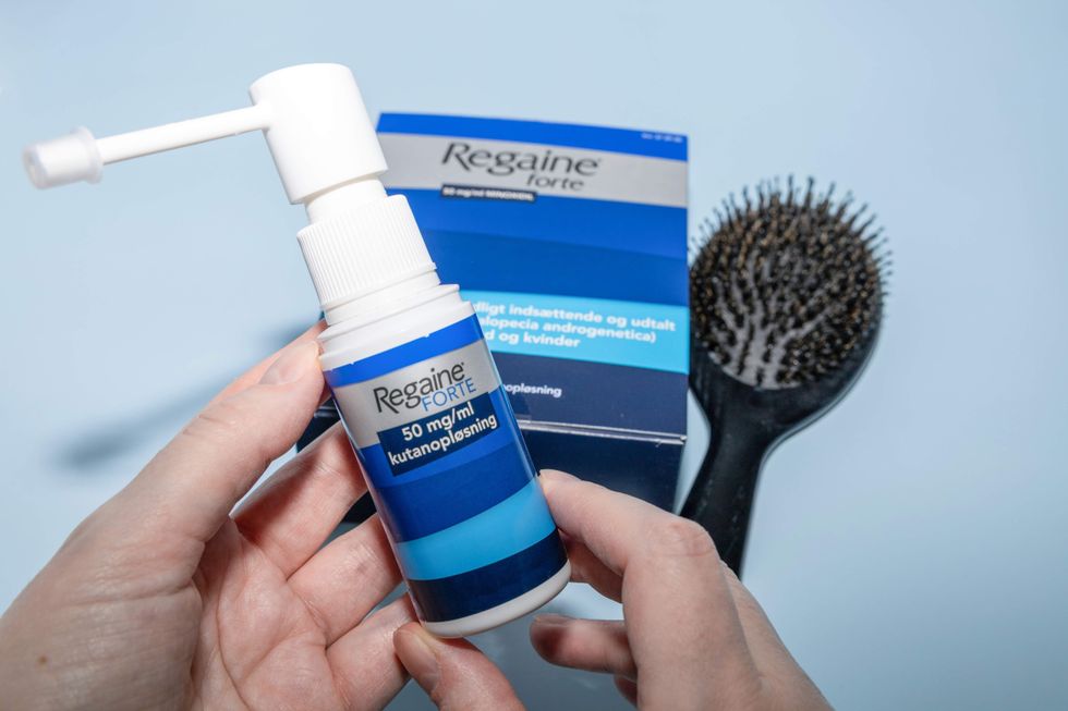 A hand holding a bottle of topical hair loss medication.
