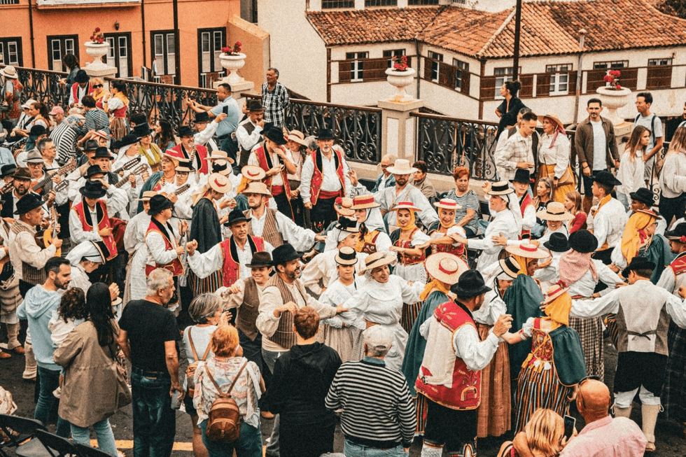 A large crowd gathers for a traditional celebration in Spain, with participants wearing colorful regional clothing.