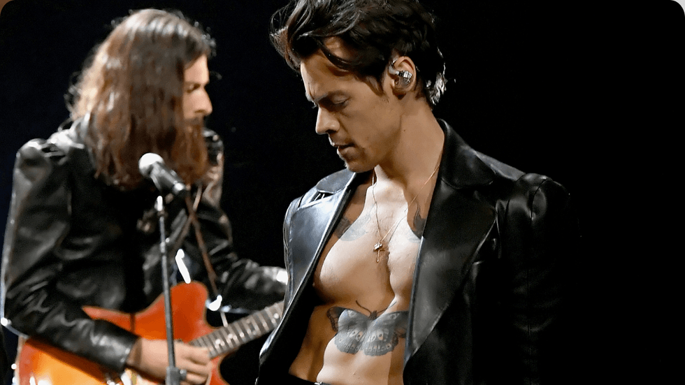 A man wearing a black leather blazer on-stage with no shirt on under.