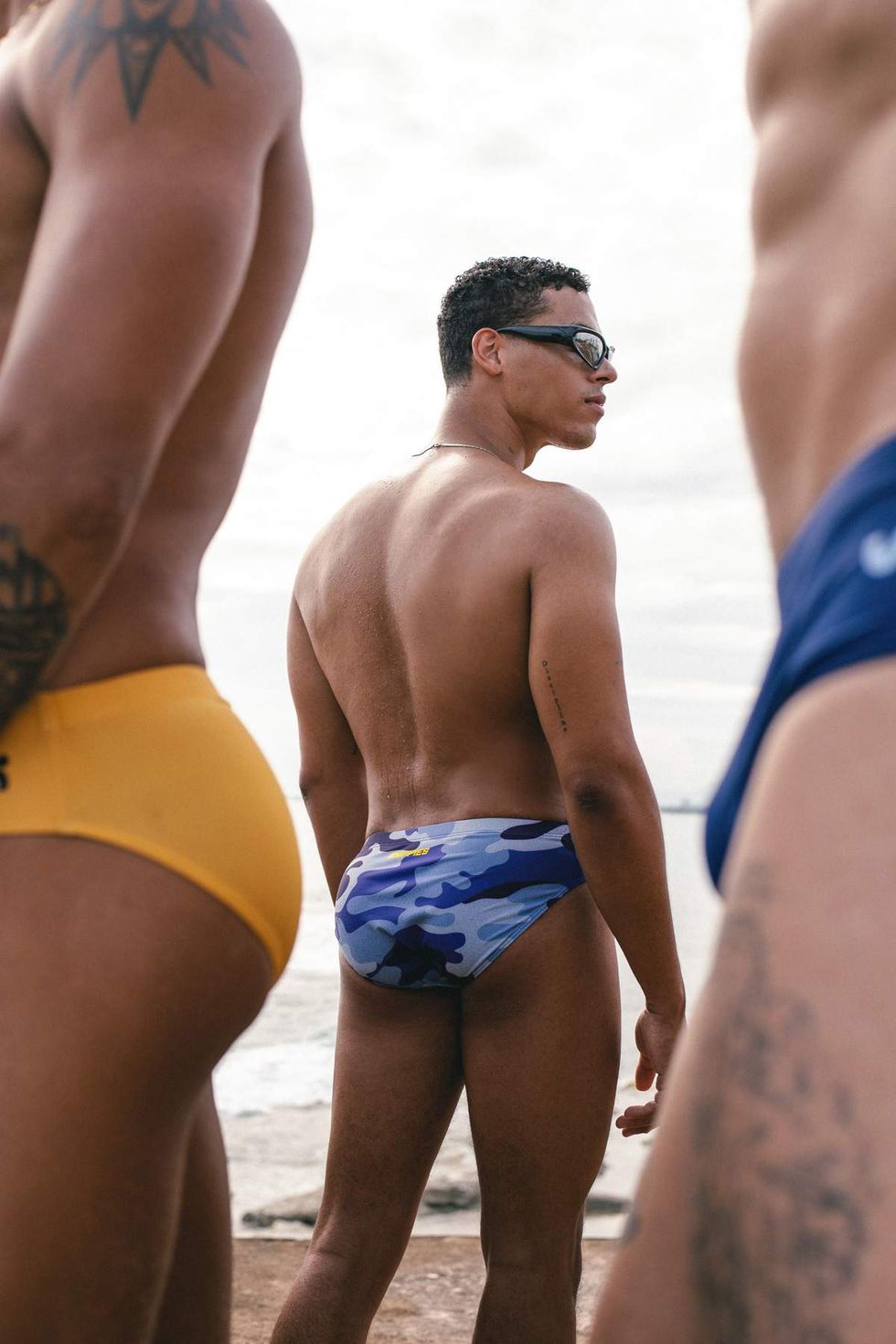 A model wearing Sniffies camo swim briefs stands near the beach during the Sniffies Summer Swim Collection campaign in Puerto Rico