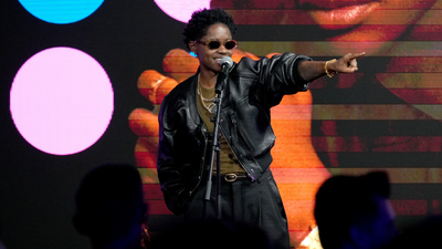 A person onstage in front of a microphone, pointing to the crowd