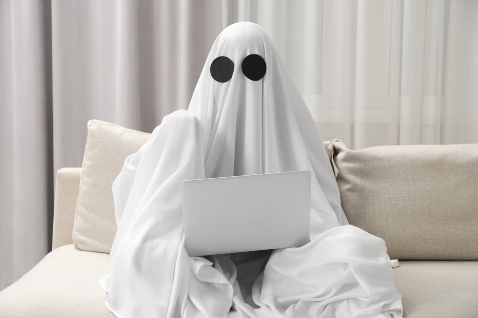 A person wearing a ghost costume using a laptop