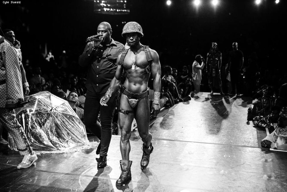 A shirtless man in army inspired gear on the runway.