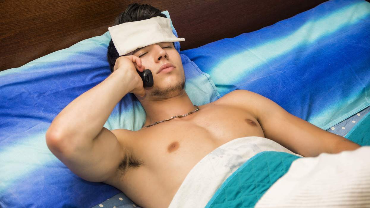 A shirtless man in bed with a towel on his forehead