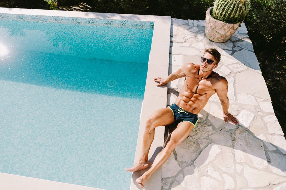 A shirtless man sunbathing beside a pool