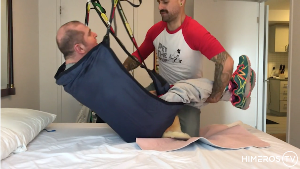 A still of a porn film featuring two performers, with one in a sling to get out of his wheelchair.