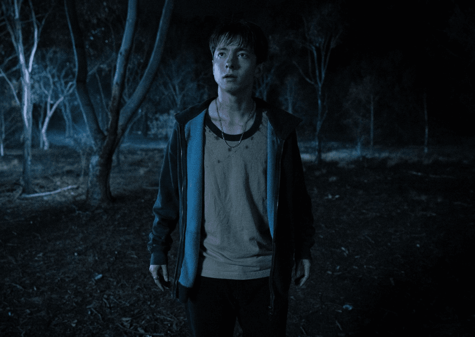 A teenage boy stands alone in a dark forest at night in a scene from Leviticus