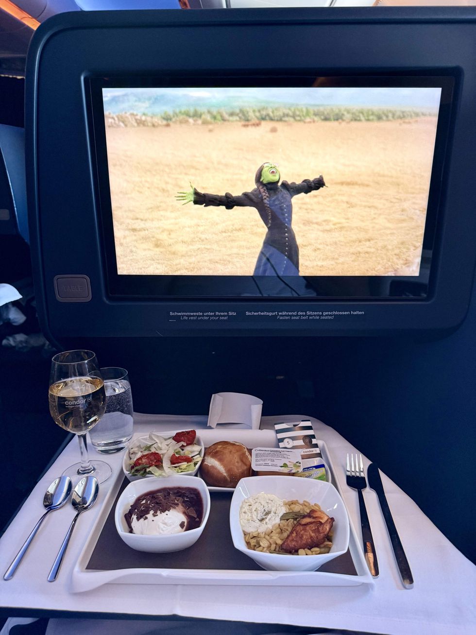 A tray of food in front of a monitor with a glass of champagne and glass of water