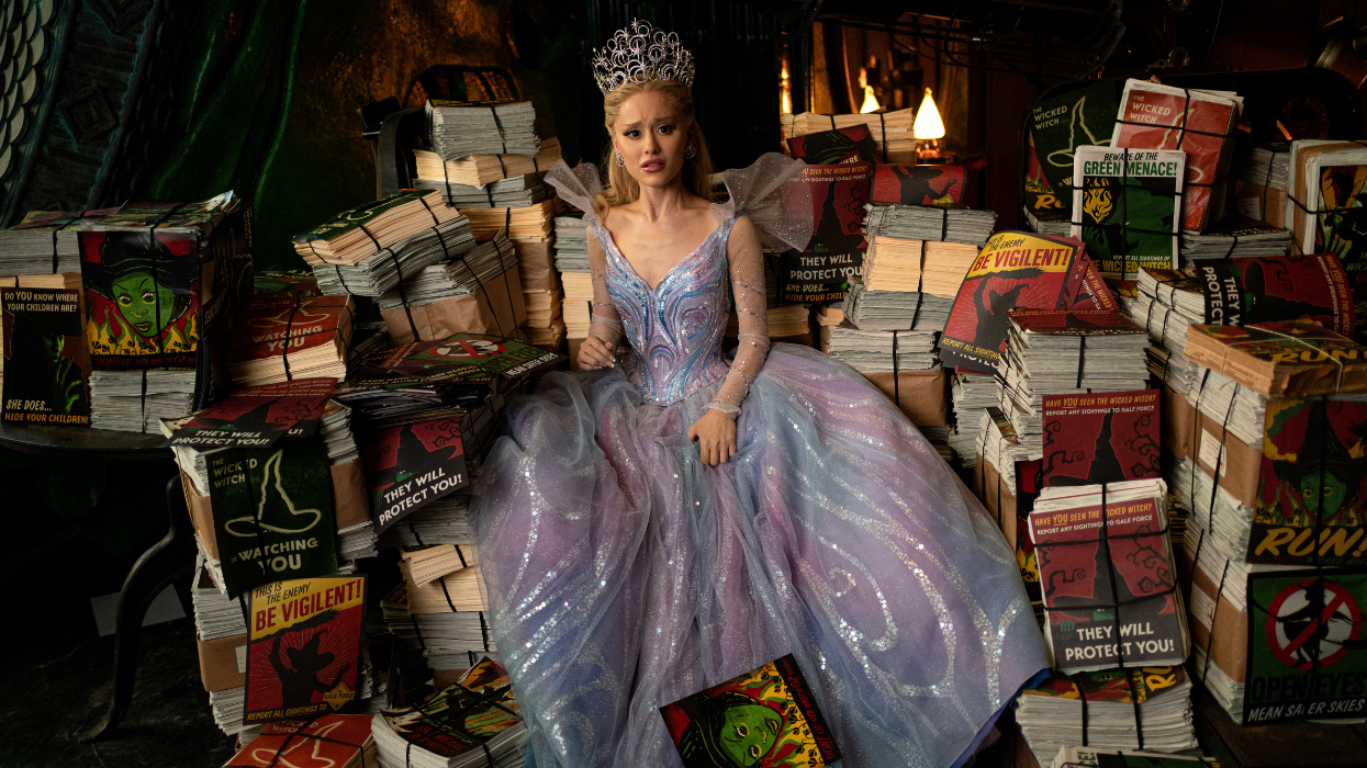 A woman sitting on multiple stacks of paper in a purple and blue gown with a crown.