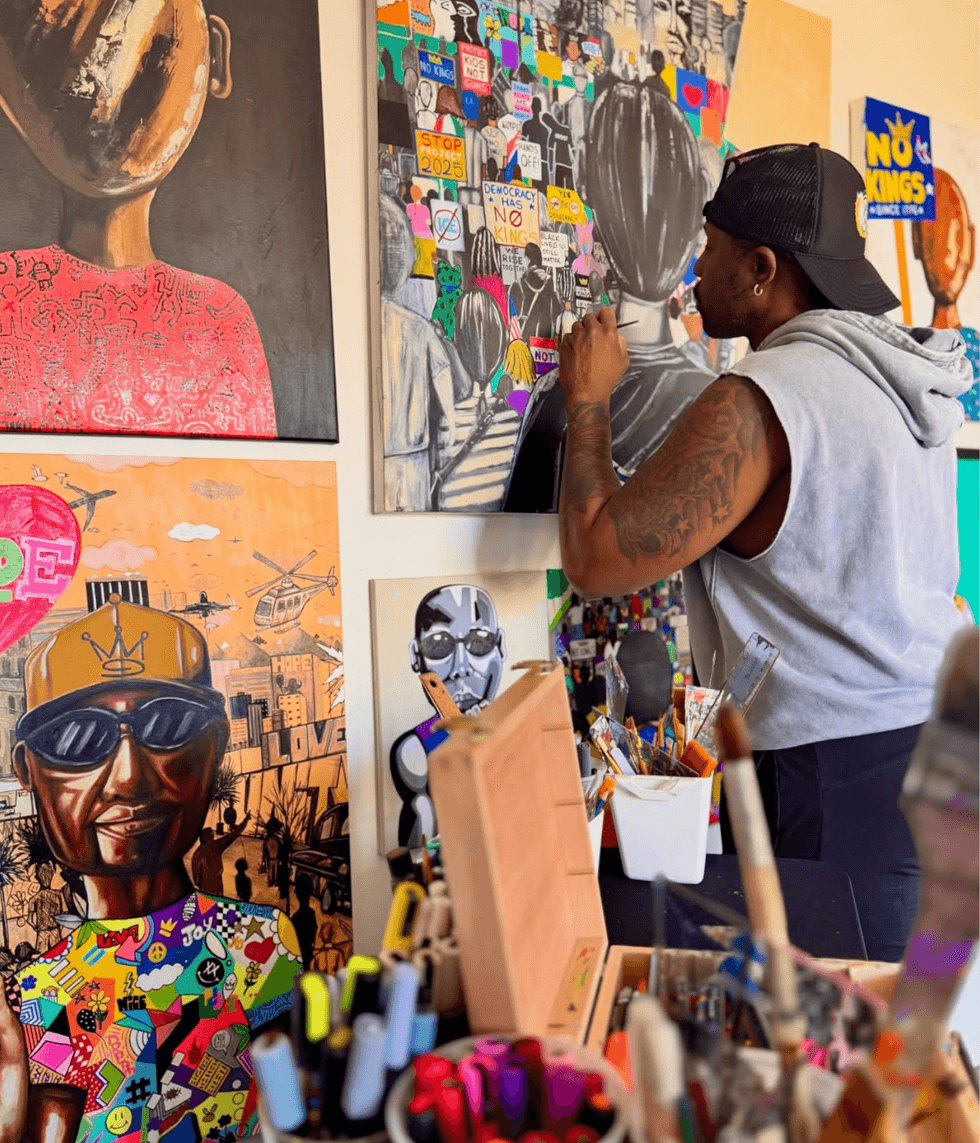 Aaron Allen Marner paints a large canvas in his studio, surrounded by colorful artworks and art supplies