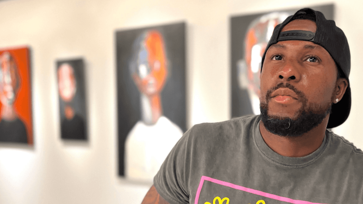 Aaron Allen Marner stands in a gallery space with blurred portraits behind him, looking off to the side