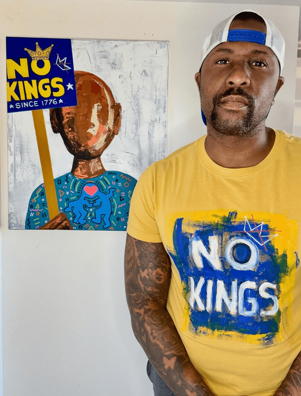 Aaron Allen Marner stands in front of a painting featuring a \u201cNo Kings\u201d protest sign
