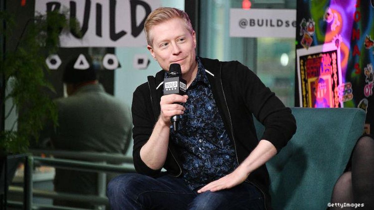 Actor Anthony Rapp on stage with a mic smiling.