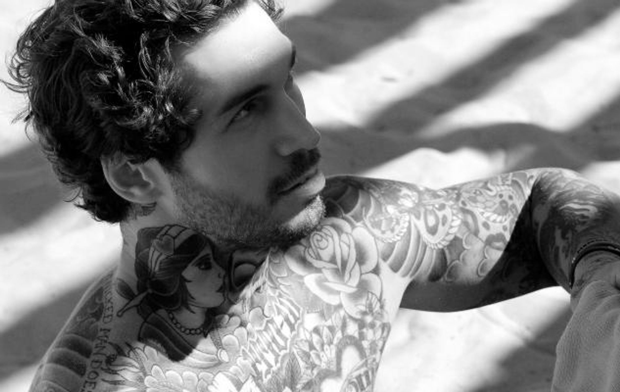 Alex Minsky reclining in a distinct editorial photograph showing his tattooed shoulder, chest and arm