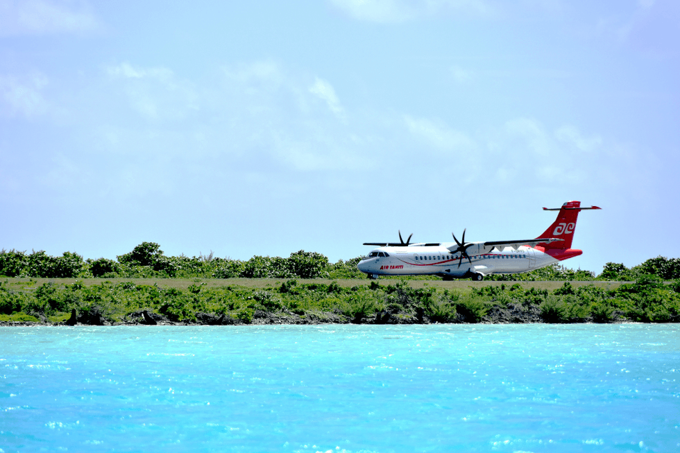 An Air Tahiti airplane sits on a runway beside bright turquoise water