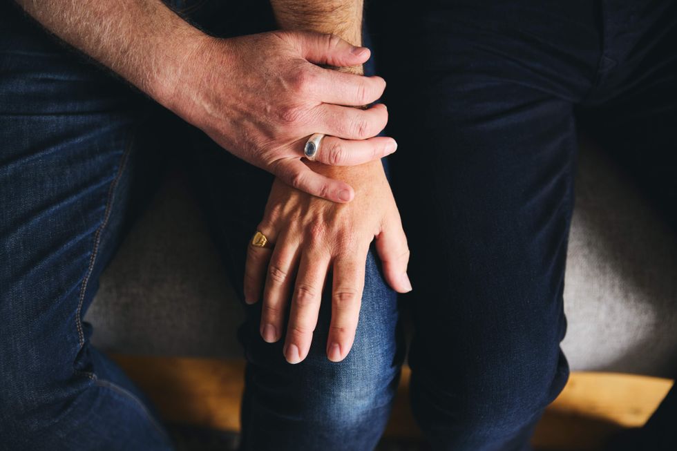 An older man's hand holding another man's hand on top of his thigh.