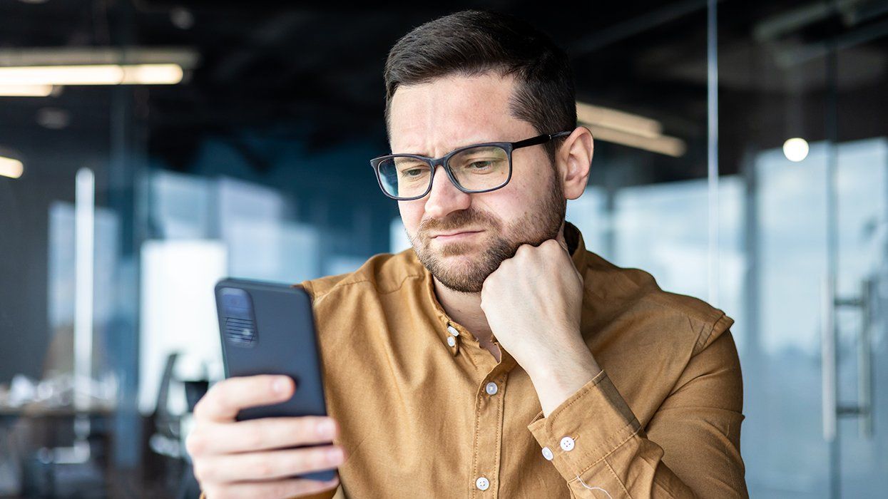 annoyed bearded man with glasses at work looking at cell phone