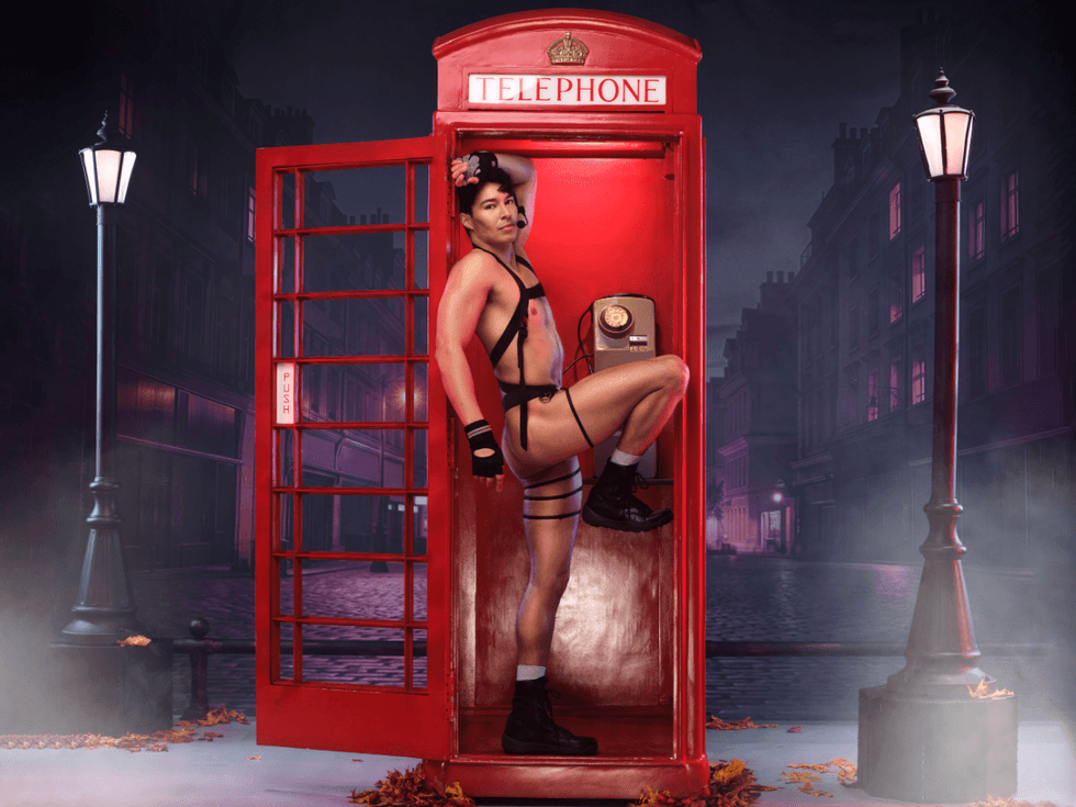 Anthony Sanchez dressed as Ethan Hunt stands in front of a red London phone booth wearing an open white shirt and black harness on a moody nighttime street