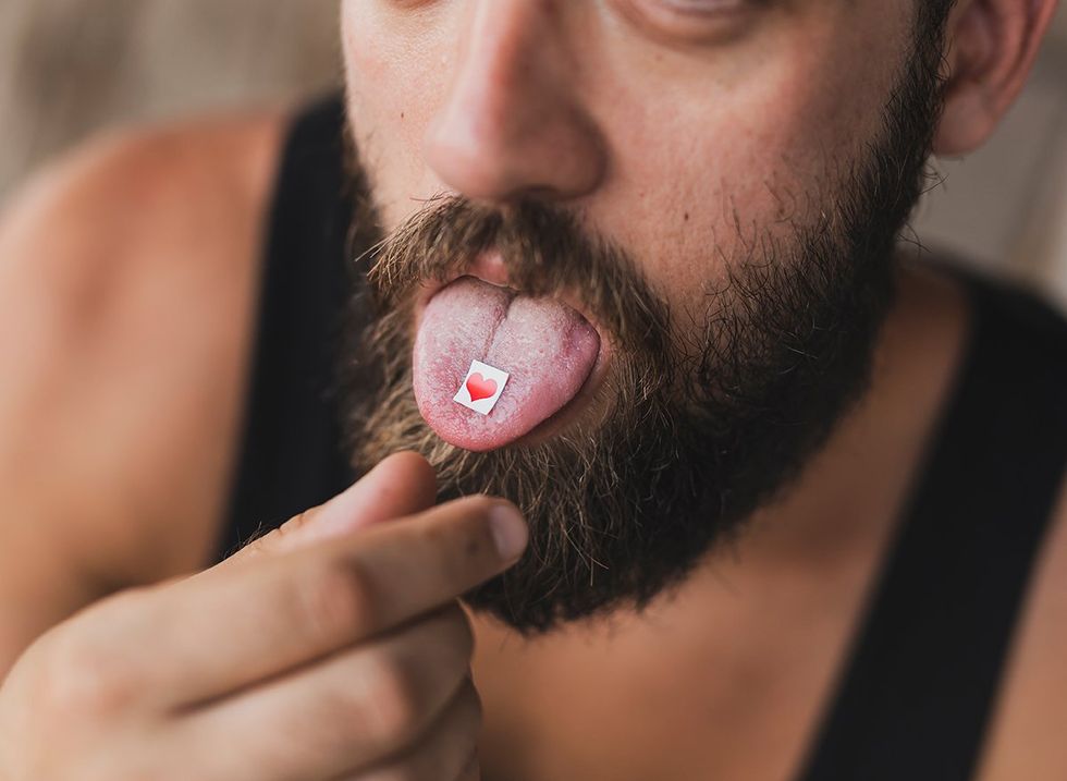 bearded man placing heart shaped paper LSD tab on his tongue