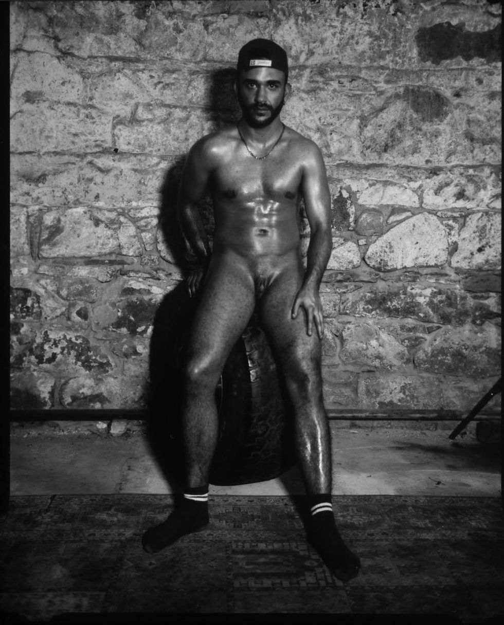Billy Vega, a trans man, posing nude against a stone backdrop.
