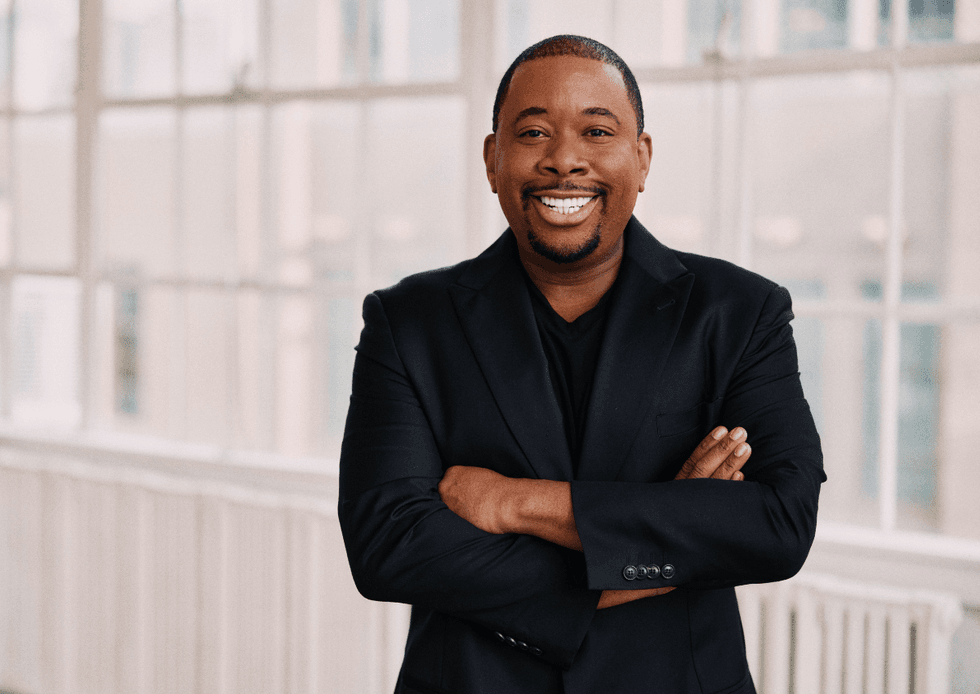 Brian Anthony Moreland standing with his arms crossed, smiling and wearing a black suit