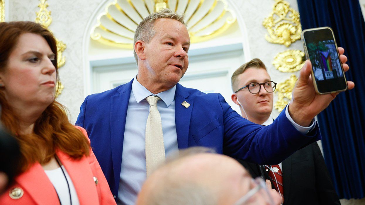 Brian Glenn White House correspondent for Real Americas Voice asks US President Donald Trump a question while holding up a cellphone photo of progress pride LGBTQIA flag