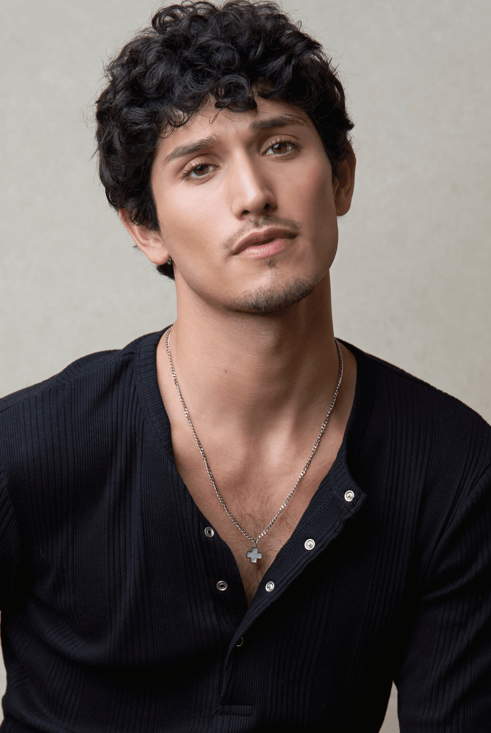 Close-up of Jacob Martinez wearing a black henley shirt and a cross necklace, looking at the camera