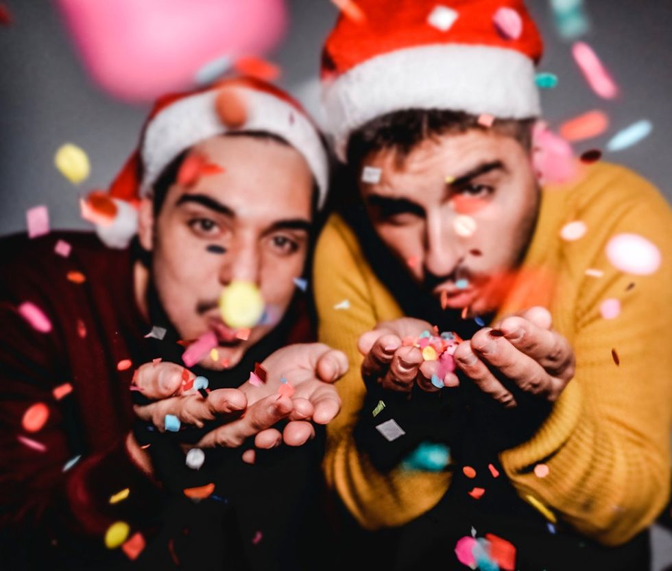 cute gay men in christmas hats blowing confetti