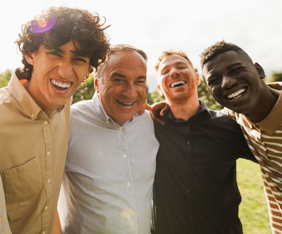 diverse group of men various age and race hugging smiling in the sunshine