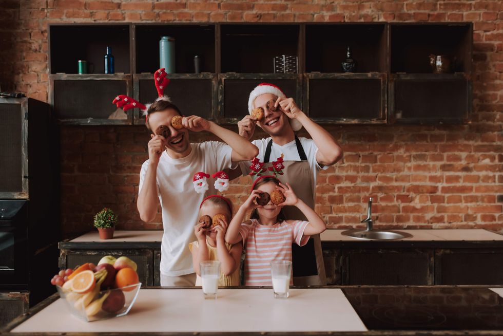 Family with festive hats holding cookies to their eyes in a kitchen.