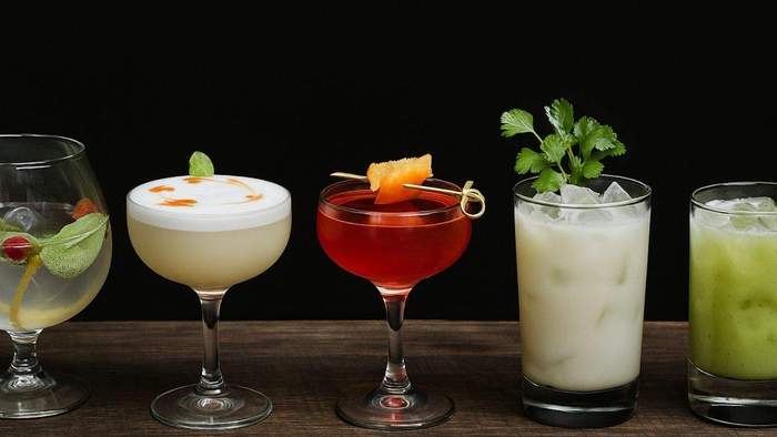 Five colorful cocktails with garnishes on a wooden surface against a black background.