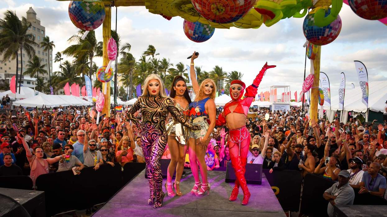 Four drag performers on stage with a lively crowd and colorful decorations.