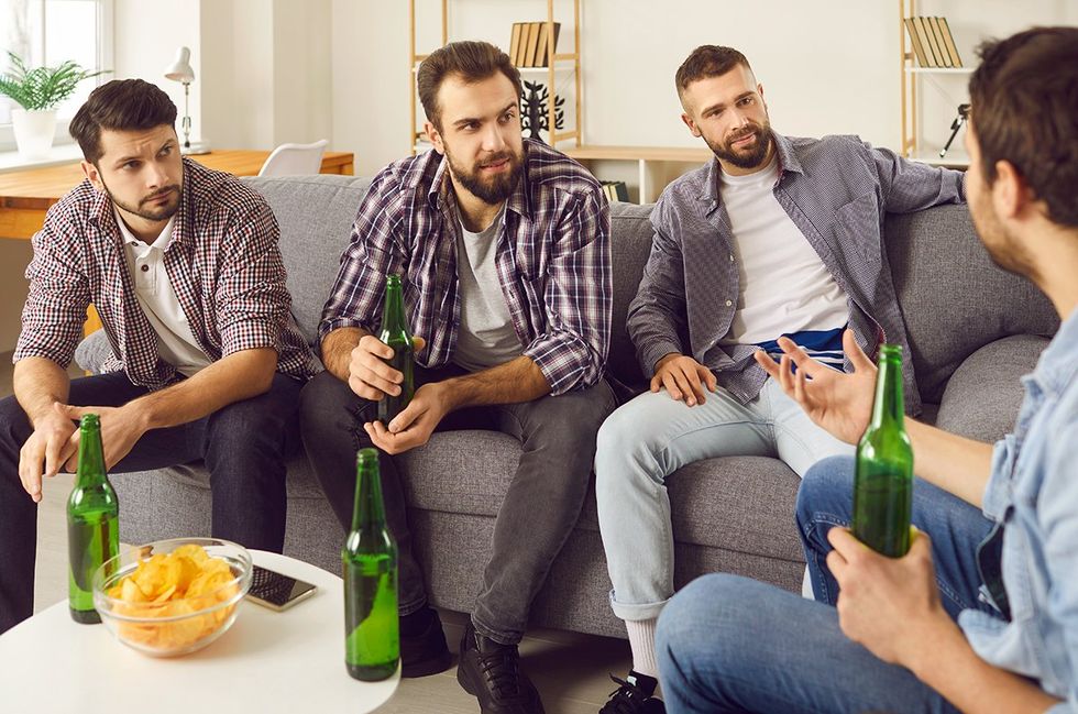 four handsome bearded men with chips and drinks sitting on couch discussing safety and boundaries