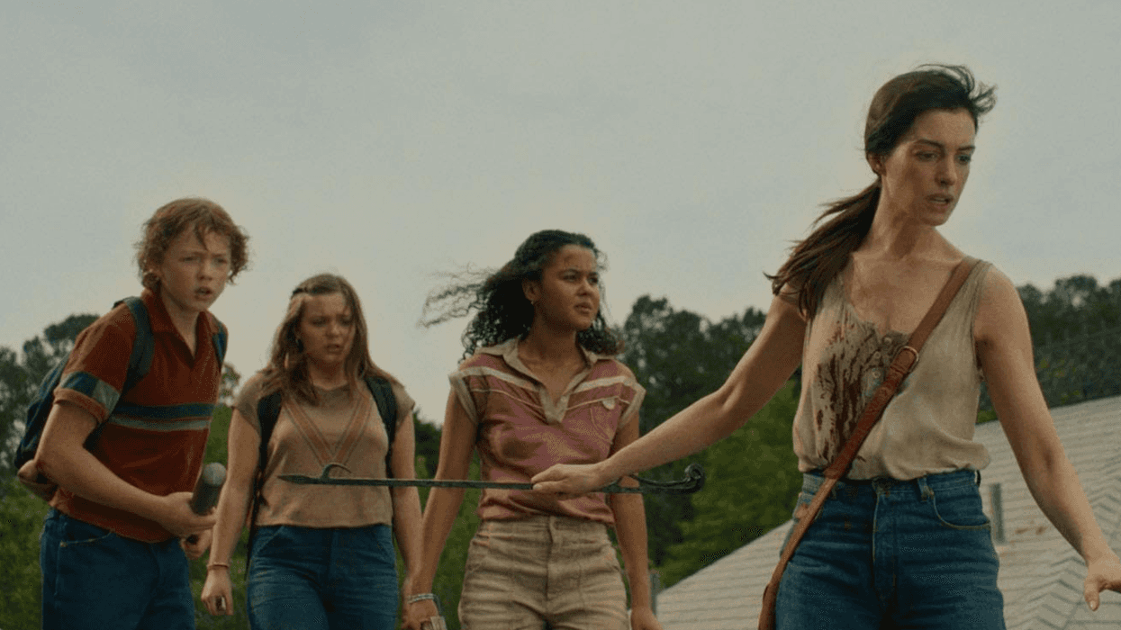 Four people on a roof, one holding a crowbar, with trees in the background.