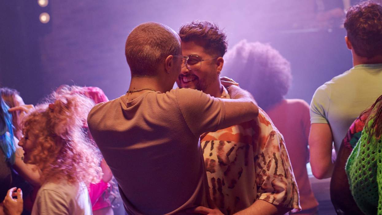 Gay couple embracing amongst a crowd of people.