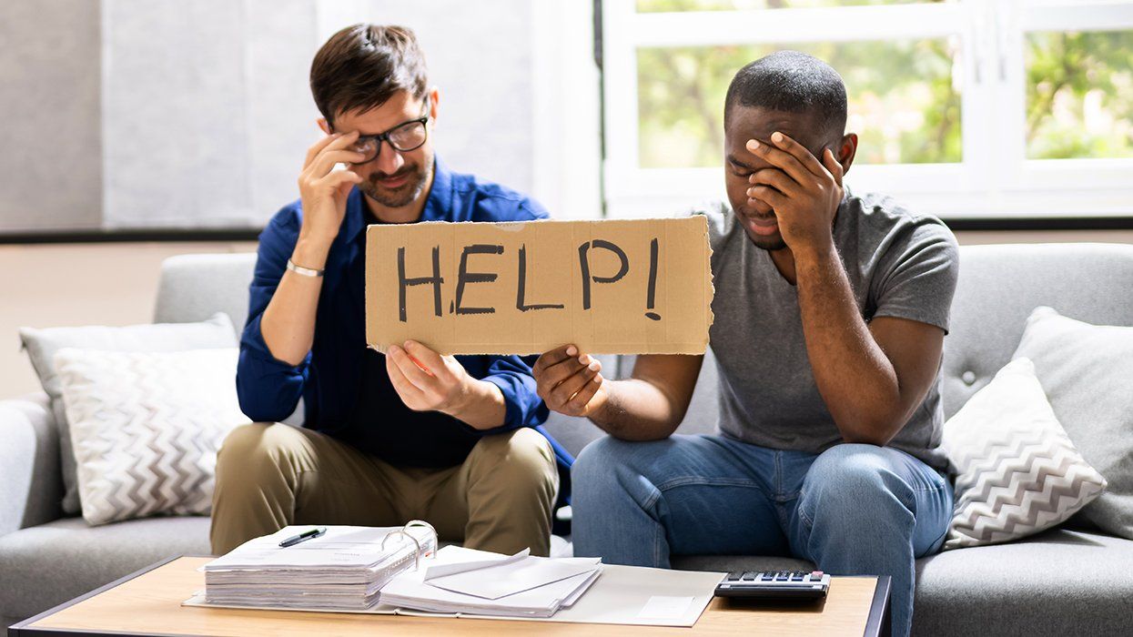gay couple sitting on a couch going over finances holding HELP sign