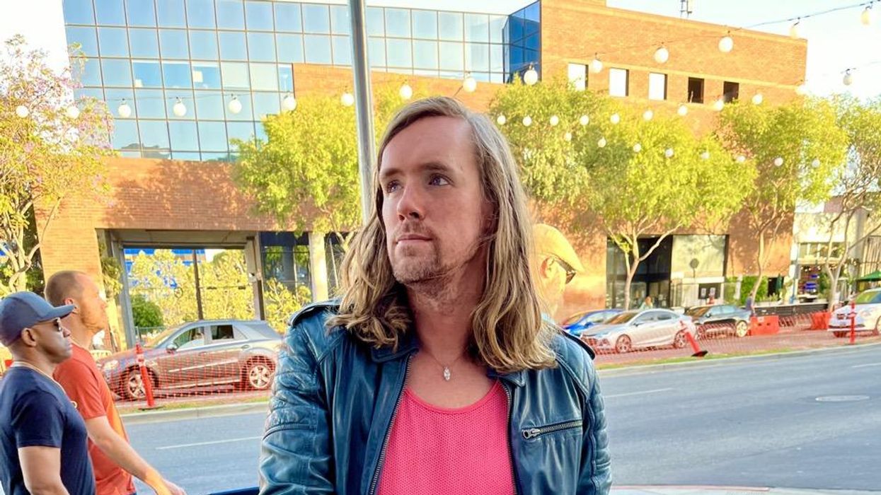 Genderfluid individual sitting outside a bar in Los Angles, their legs are crossed and they are wearing rainbow boots