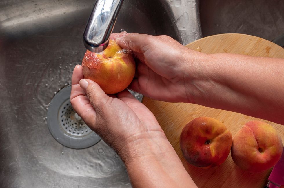 Hands washing peaches in the sink