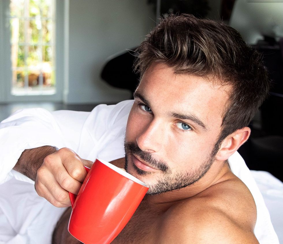handsome man blue eyes looking contemplatively at the camera holding a red coffee mug