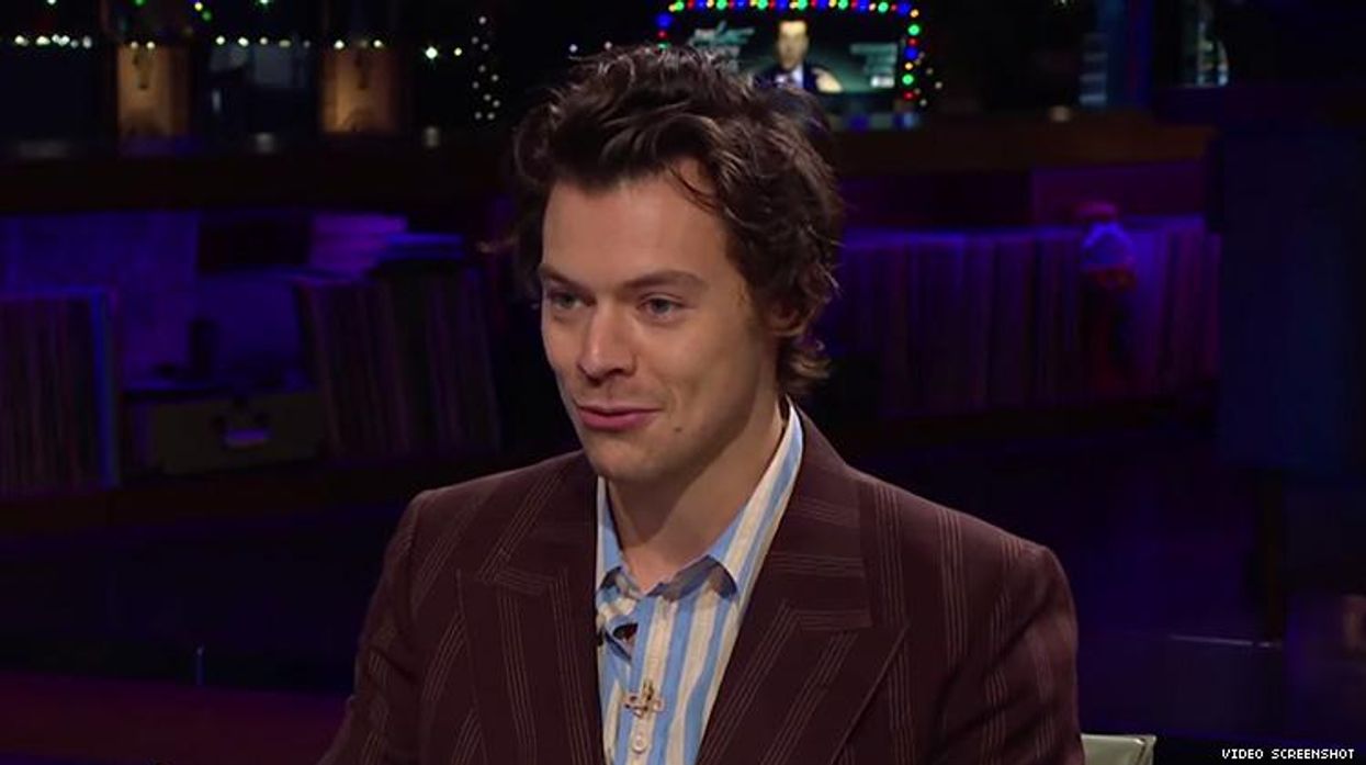 Harry Styles in a suit sitting at a table.