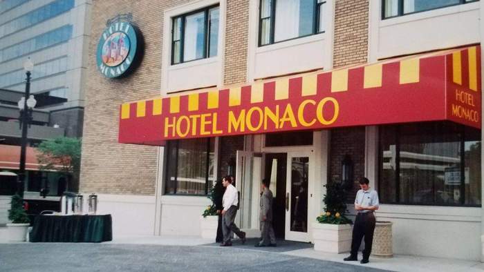 Hotel Monaco entrance with red and yellow awning, two men walking out.