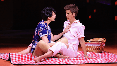 Jenn Colella and Lauren Patten sit together on a red picnic blanket during a performance at Broadway Backwards.