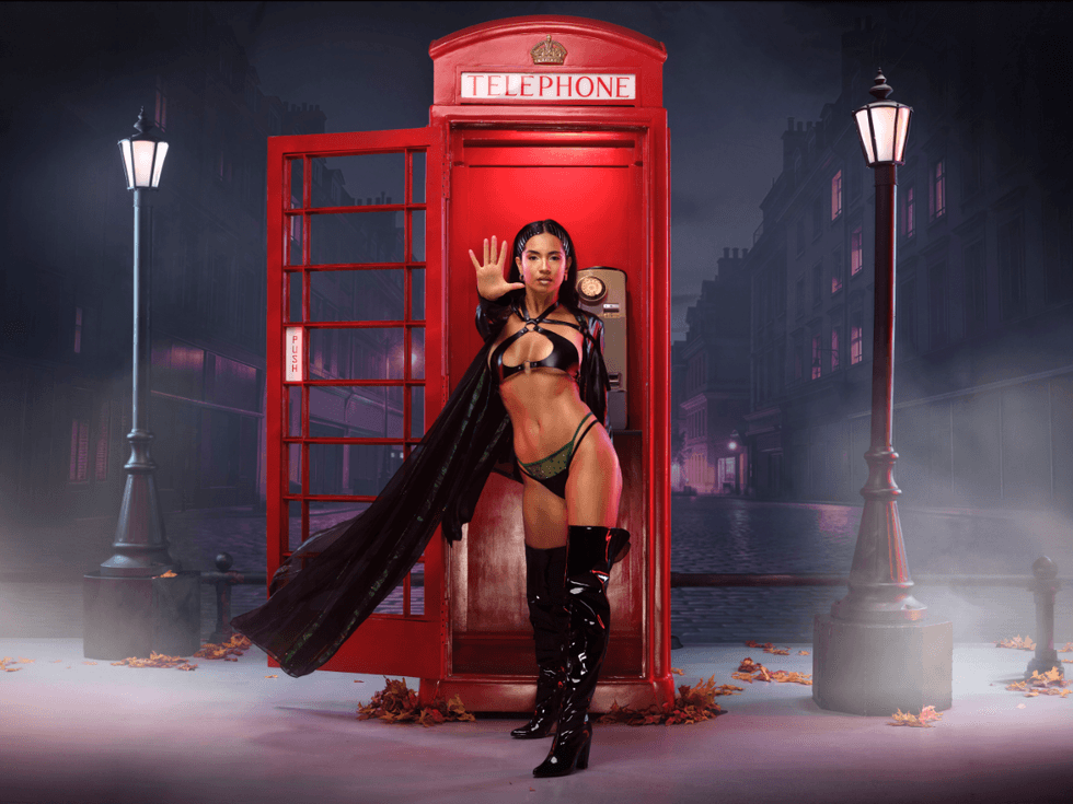 Jessica White poses in front of a red London phone booth dressed as Trinity from The Matrix, wearing a black leather-inspired outfit and thigh-high boots on a moody city street