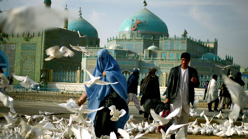 Kabul Afghanistan women in burqas and men with traditional dress outside a mosque surrounded by white birds