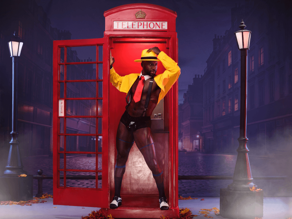 Khasan Brailsford poses inside a red London phone booth dressed as Dick Tracy, wearing a bright yellow hat and coat with a red tie against a foggy city street at night