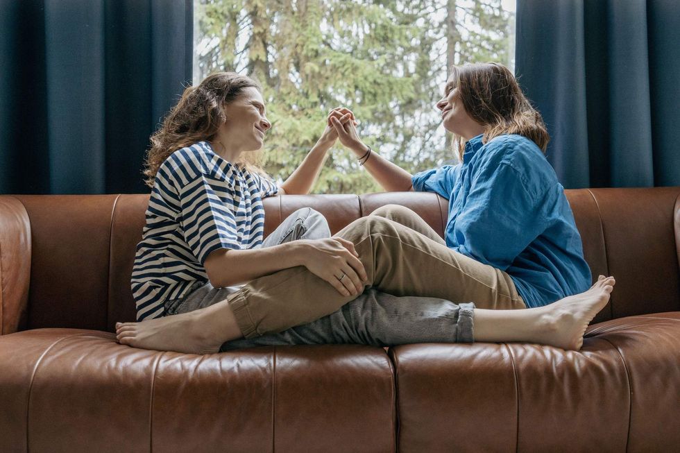 Lesbian sitting on a couch holding hands with their legs intertwined
