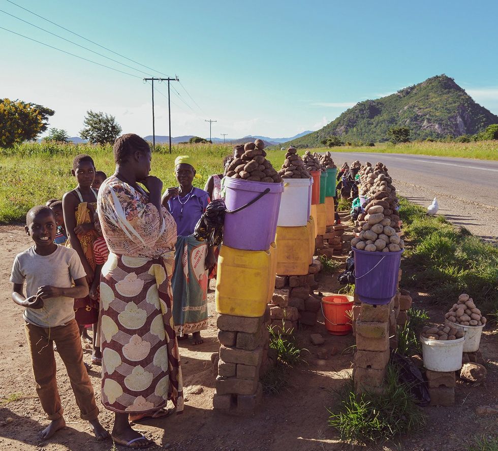 LILONGWE MALAWI AFRICA African women and children are smiling and selling potatoes along the road to Dedza